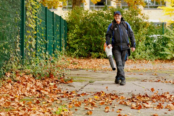 Mitarbeiter bei der Arbeit. Es wird Laub weggeblasen